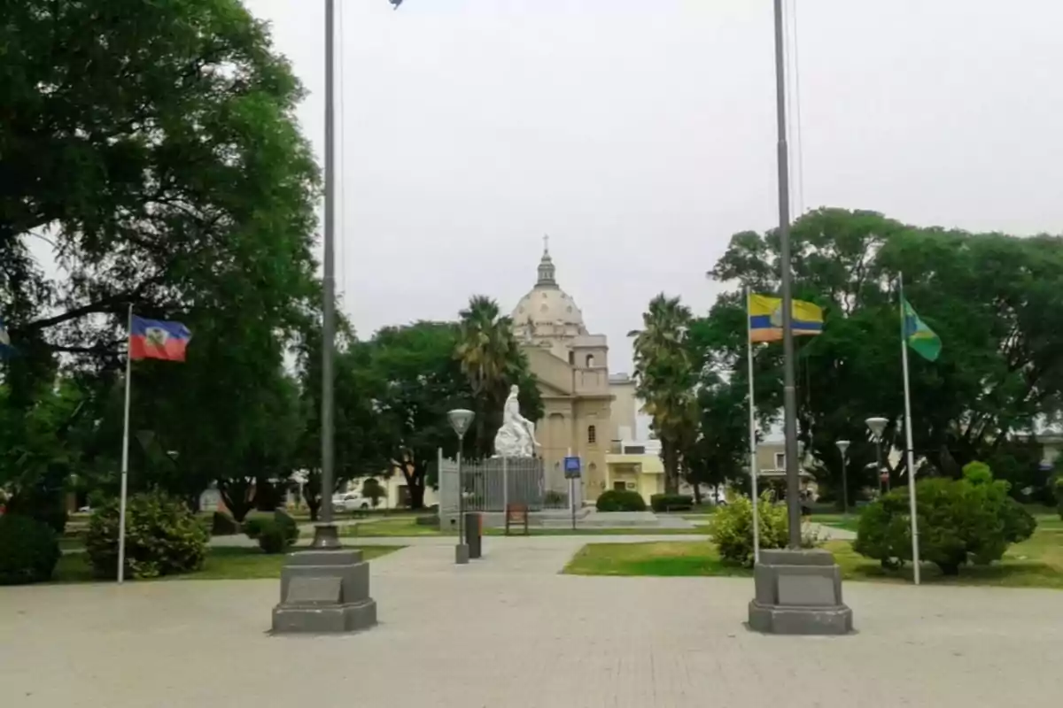 Central square with a white statue surrounded by trees and flags, in the background a large-domed church can be seen. Central square with a white statue surrounded by trees and flags, in the background a large-domed church can be seen.