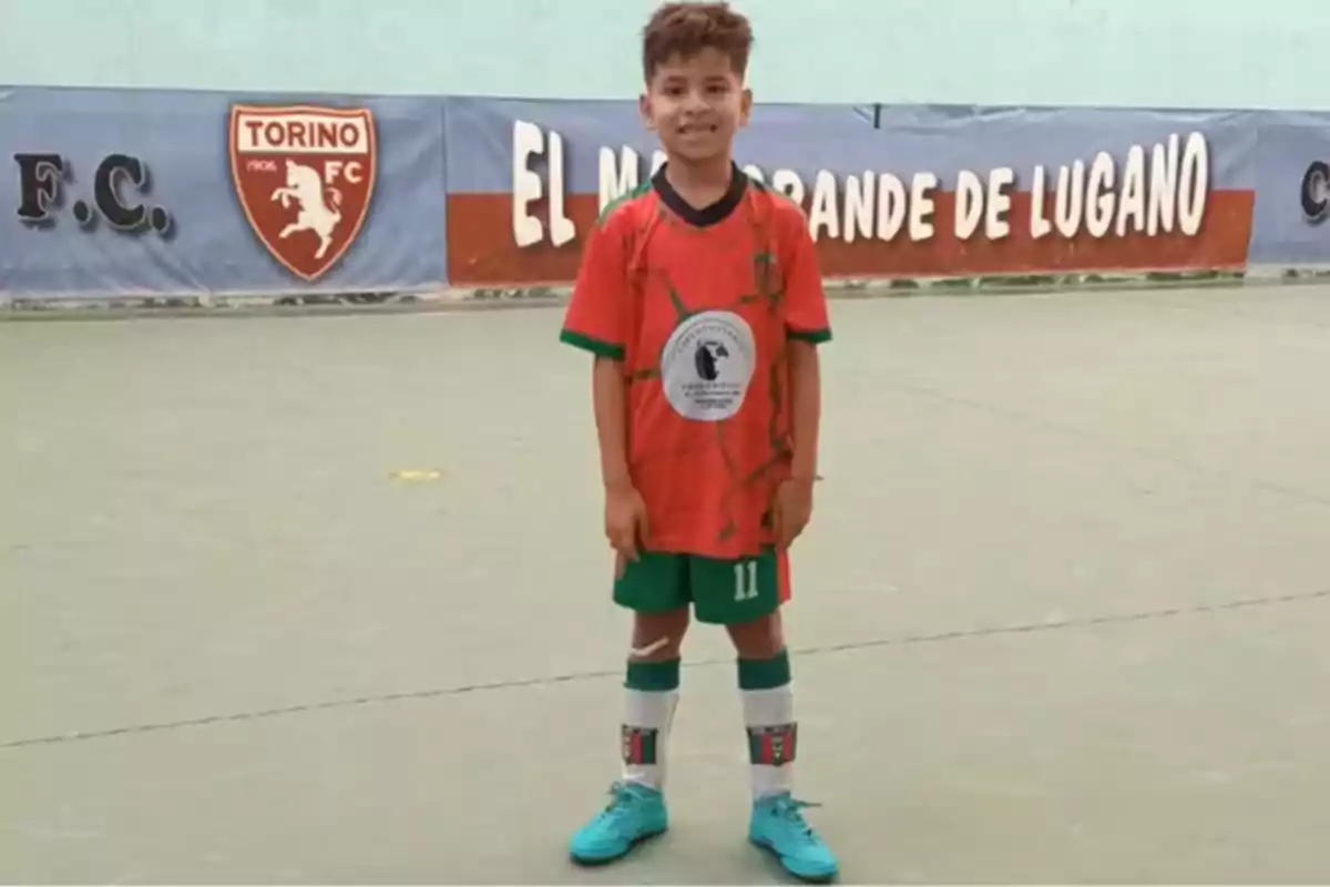 Boy in an orange and green soccer uniform posing on an indoor field with a sign in the background that says Boy in an orange and green soccer uniform posing on an indoor field with a sign in the background that says
