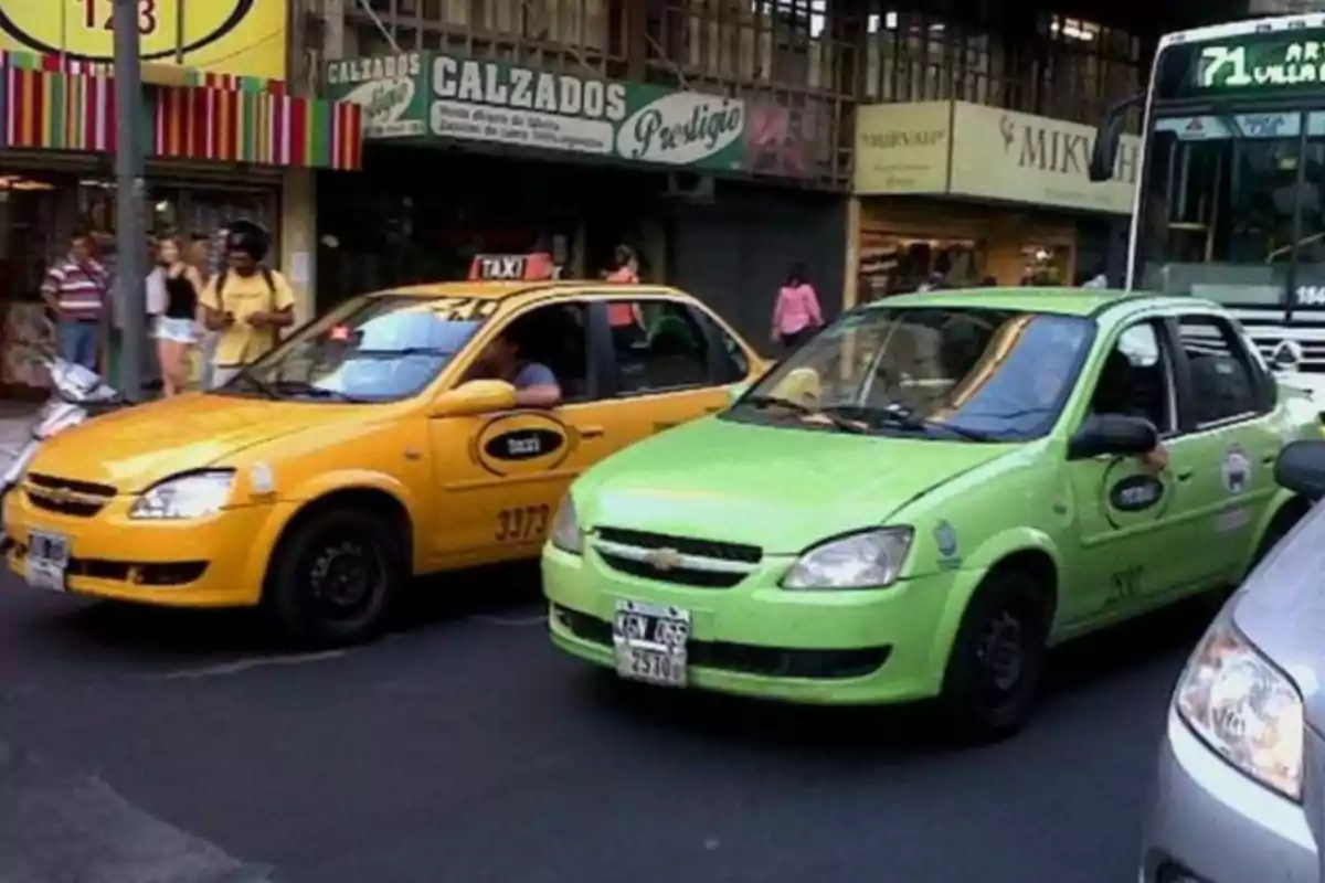 Two Chevrolet taxis of the same model, one yellow and one green, are stopped on a busy street with people walking and a bus in the background.