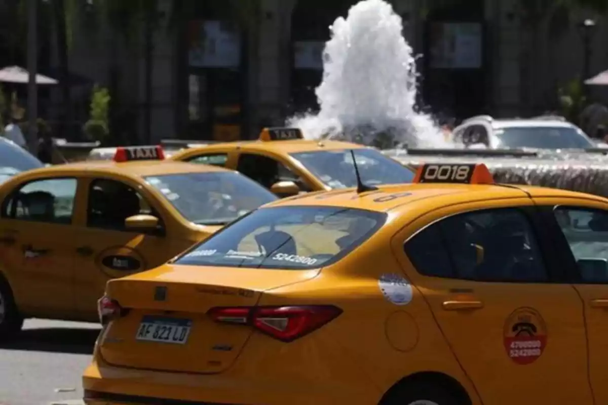 Several yellow taxis are parked near a water fountain in a city. Several yellow taxis are parked near a water fountain in a city.