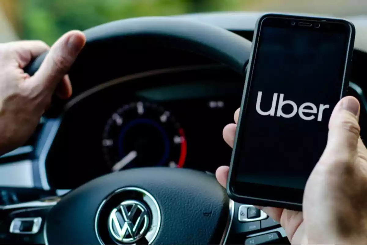 Person driving a Volkswagen car while holding a mobile phone with the Uber app open Person driving a Volkswagen car while holding a mobile phone with the Uber app open