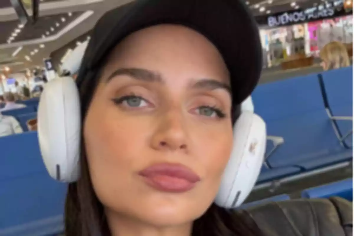Woman with white headphones and a black cap sitting in an airport waiting area