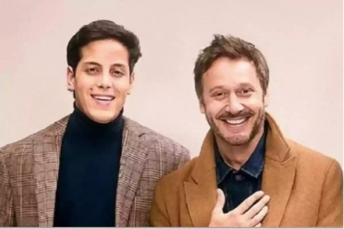 Dos hombres sonrientes posan juntos usando abrigos elegantes frente a un fondo claro