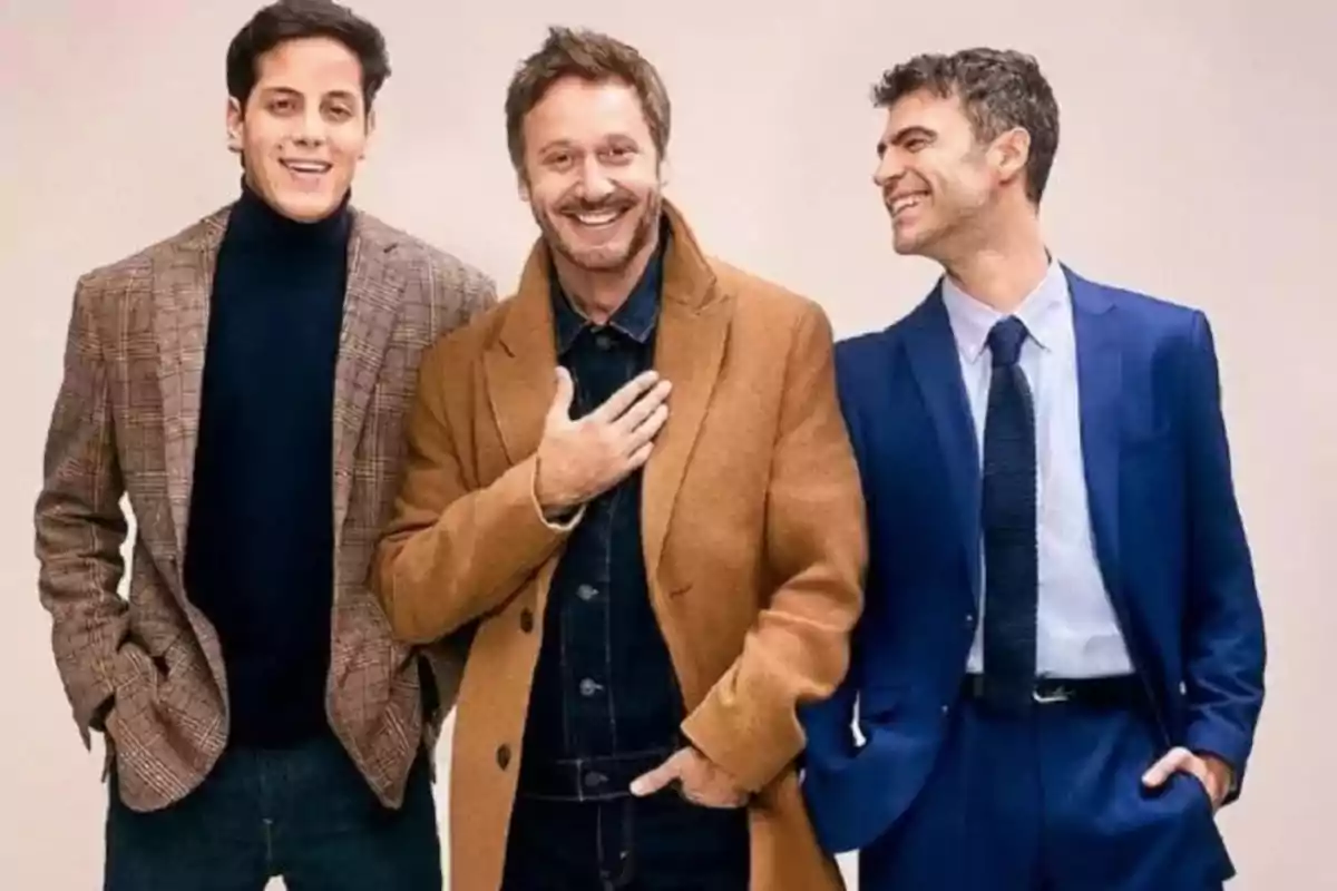 Tres hombres sonrientes posan juntos usando ropa elegante y casual en un fondo claro Tres hombres sonrientes posan juntos usando ropa elegante y casual en un fondo claro