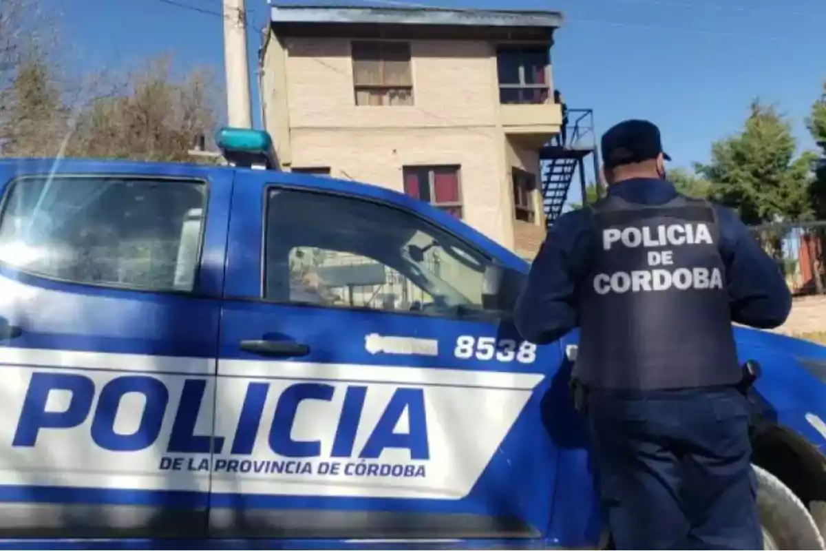 Un policía de Córdoba de espaldas junto a una patrulla azul estacionada frente a una casa