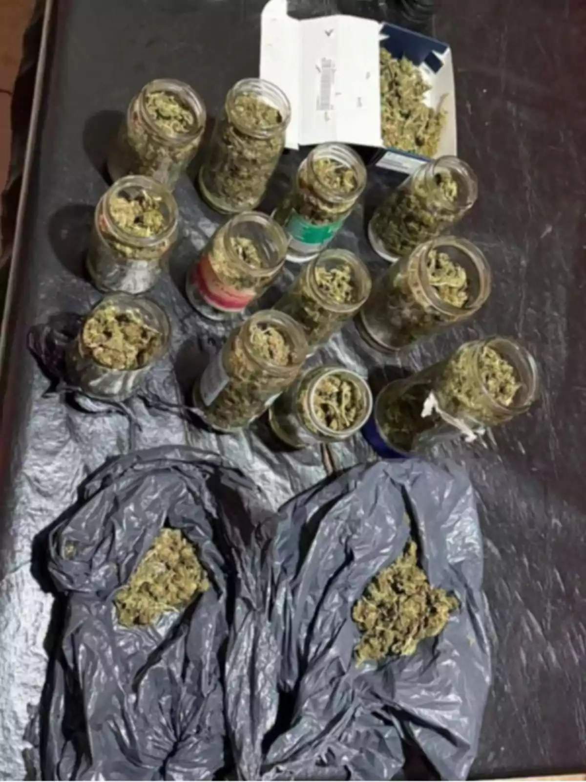 Varios frascos de vidrio y bolsas de plástico contienen lo que parece ser marihuana sobre una superficie oscura Varios frascos de vidrio y bolsas de plástico contienen lo que parece ser marihuana sobre una superficie oscura