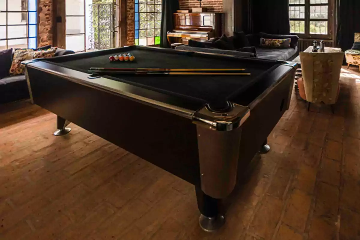 Mesa de billar negra en una sala con sofás, piano y ventanas grandes Mesa de billar negra en una sala con sofás, piano y ventanas grandes