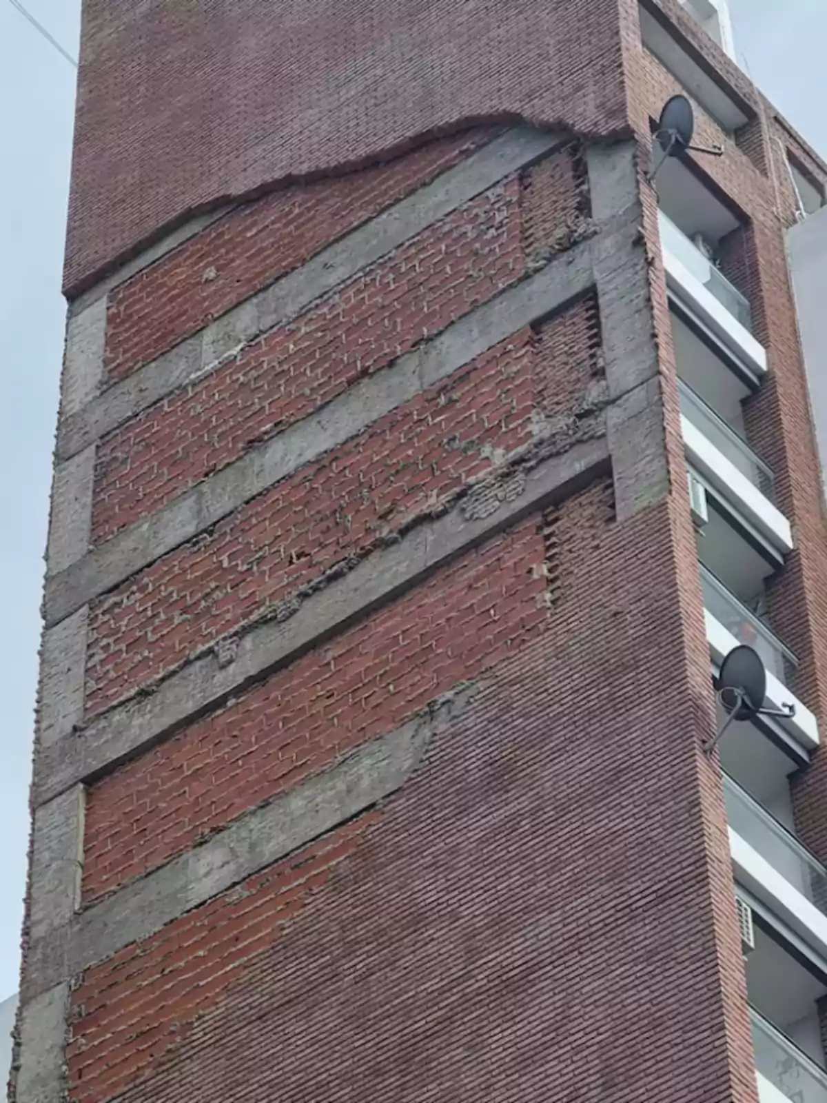 Fachada de edificio de ladrillo con parte del revestimiento desprendido dejando al descubierto la estructura y los ladrillos internos Fachada de edificio de ladrillo con parte del revestimiento desprendido dejando al descubierto la estructura y los ladrillos internos