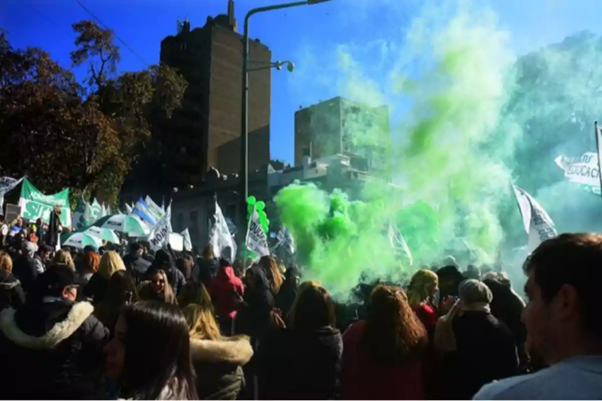 Manifestación multitudinaria en la calle con humo verde, banderas y globos, bajo un cielo azul y edificios de fondo Manifestación multitudinaria en la calle con humo verde, banderas y globos, bajo un cielo azul y edificios de fondo