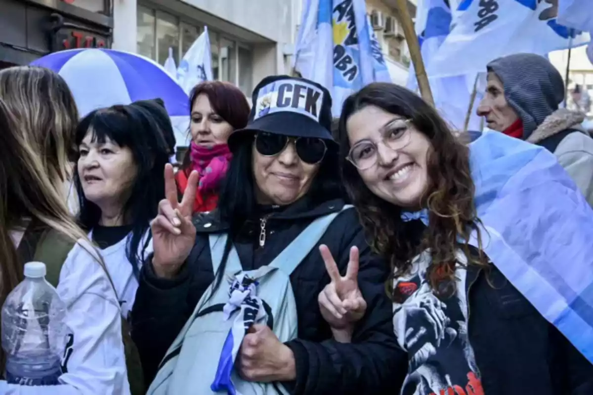 Grupo de personas en una manifestación con banderas y ropa alusiva, dos mujeres en primer plano sonríen y hacen el gesto de la victoria con los dedos. Grupo de personas en una manifestación con banderas y ropa alusiva, dos mujeres en primer plano sonríen y hacen el gesto de la victoria con los dedos.