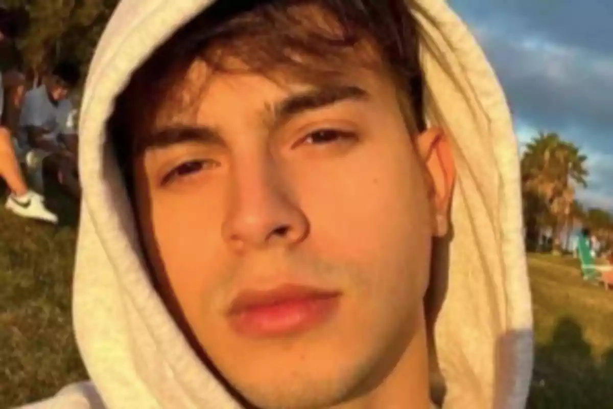 Young man in a light-colored hoodie enjoys the sunset light in a park