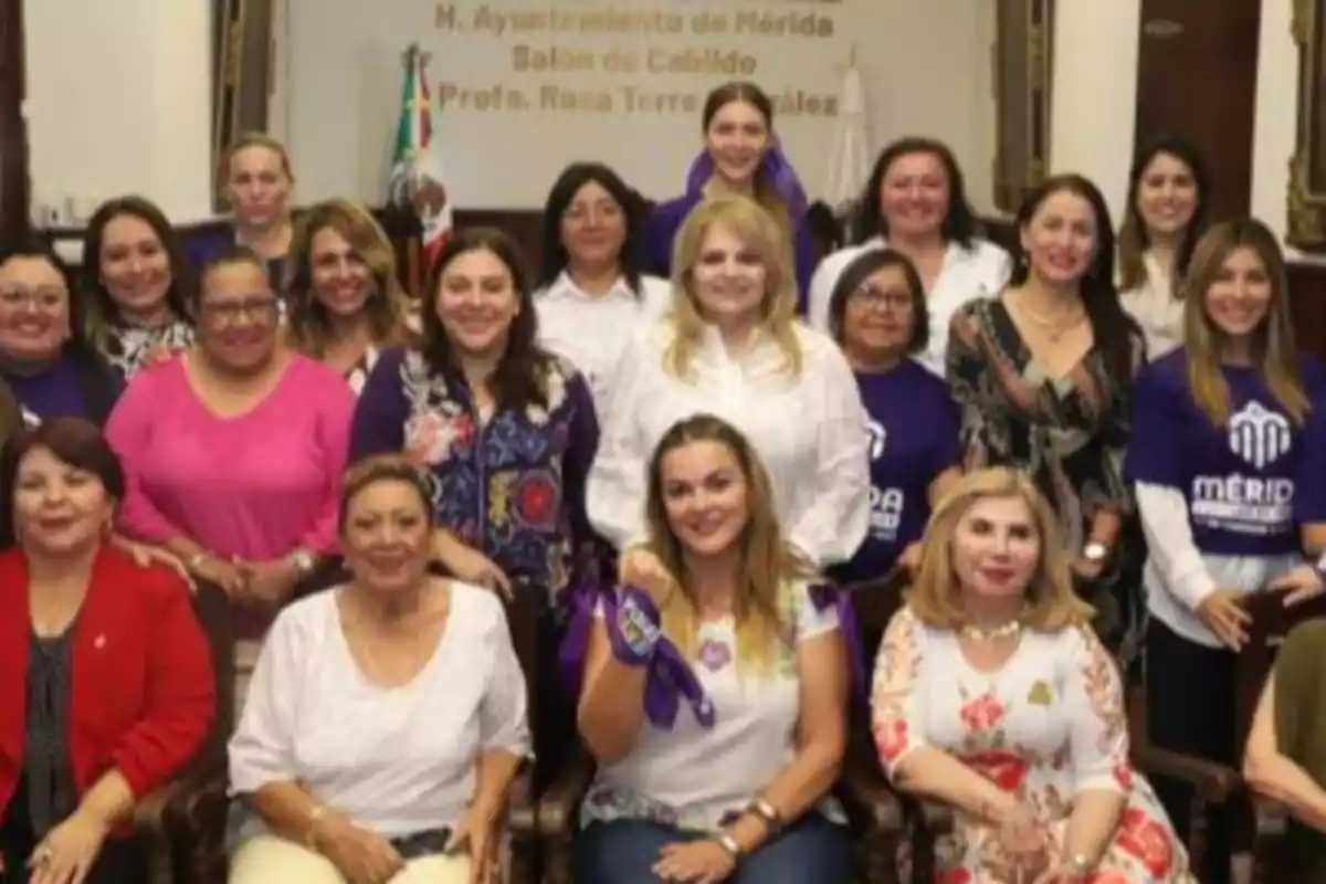 A group of women posing together in a room with a Mexican flag in the background.