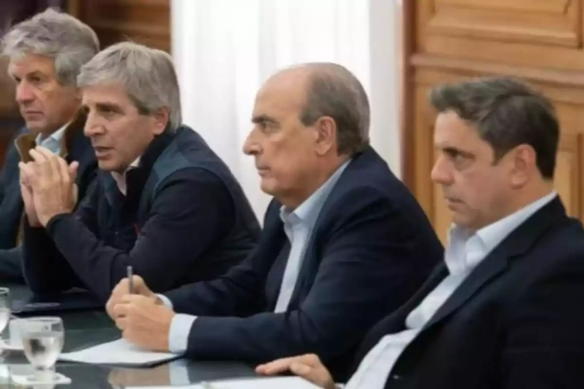 Four men dressed in suits and seated at a conference table pay attention during a meeting. Four men dressed in suits and seated at a conference table pay attention during a meeting.