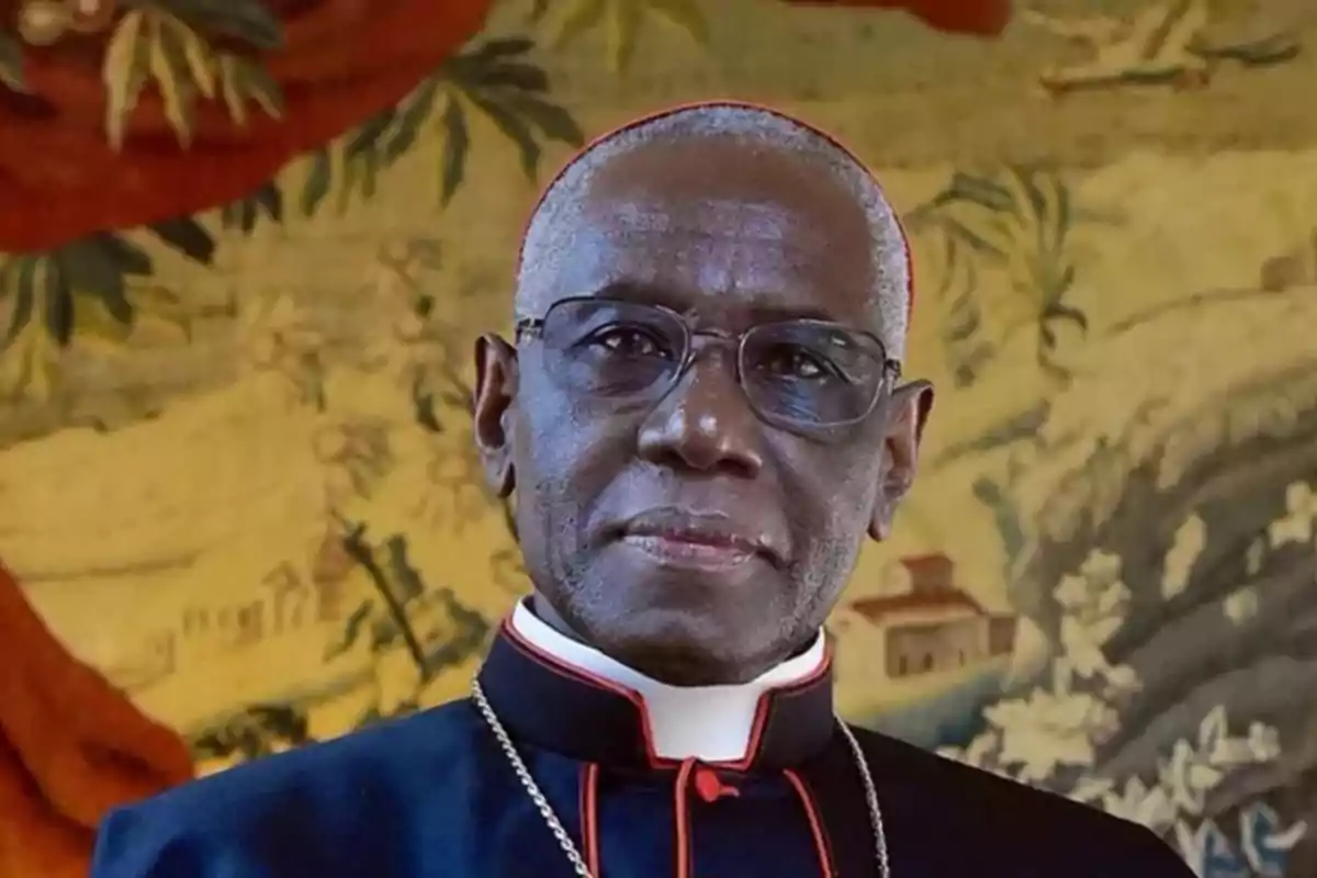 A man in religious attire and glasses in front of a decorative background. A man in religious attire and glasses in front of a decorative background.