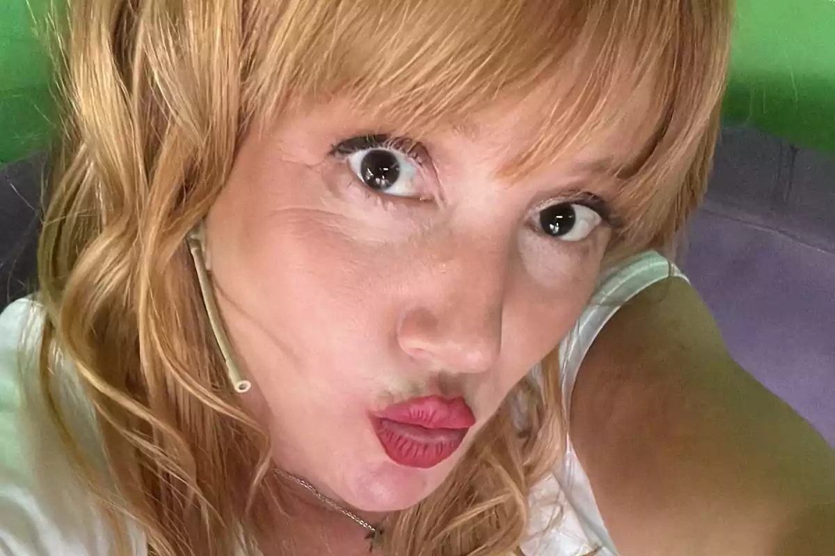 Mujer de cabello rubio rizado se toma una selfie haciendo un gesto de beso con los labios pintados de rojo y lleva un micrófono de diadema. Mujer de cabello rubio rizado se toma una selfie haciendo un gesto de beso con los labios pintados de rojo y lleva un micrófono de diadema.