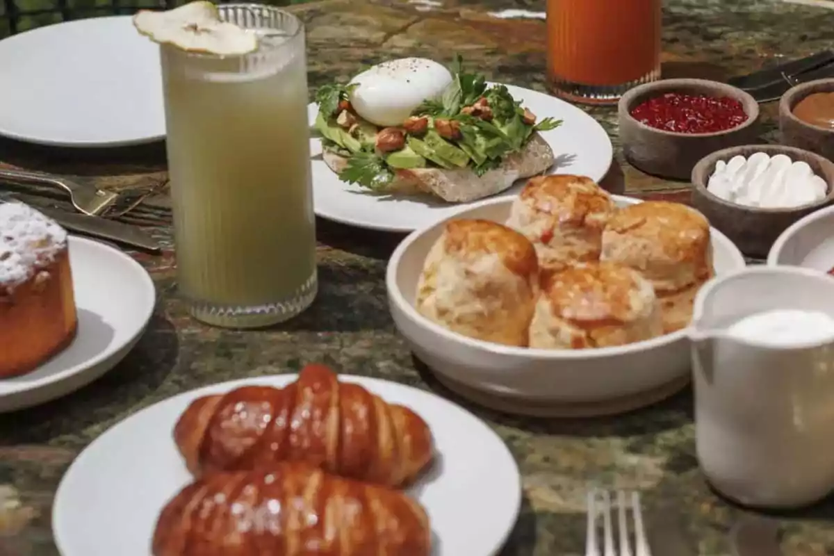 Breakfast with croissants, scones, pound cake, juices, avocado toast with egg, jam, and cream on a marble table Breakfast with croissants, scones, pound cake, juices, avocado toast with egg, jam, and cream on a marble table