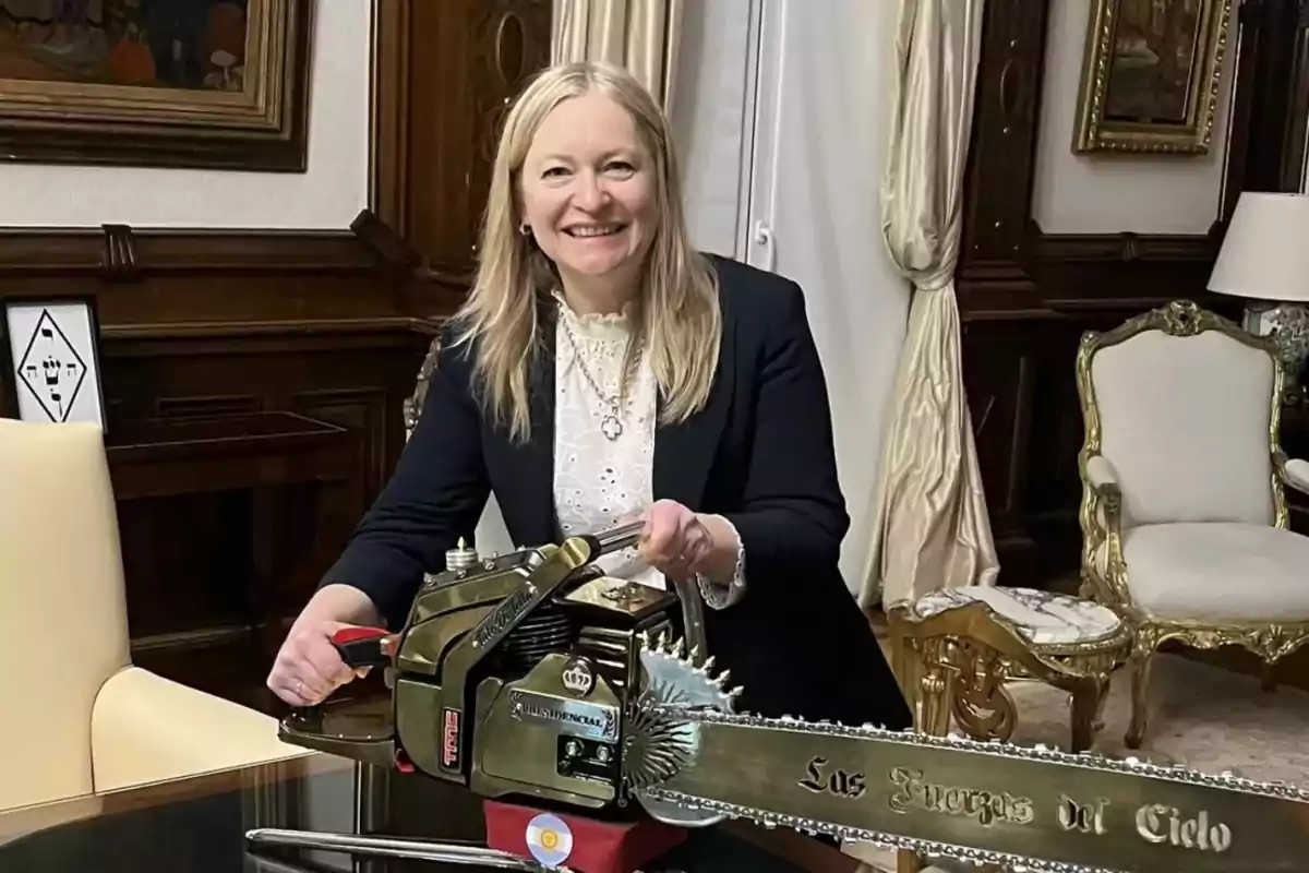 A smiling person holds a decorative chainsaw in an elegant room with classic furniture and curtains.