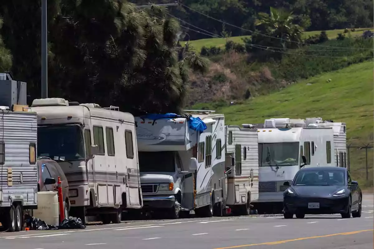 Una fila de casas rodantes estacionadas al lado de una carretera con un automóvil negro pasando por el carril.