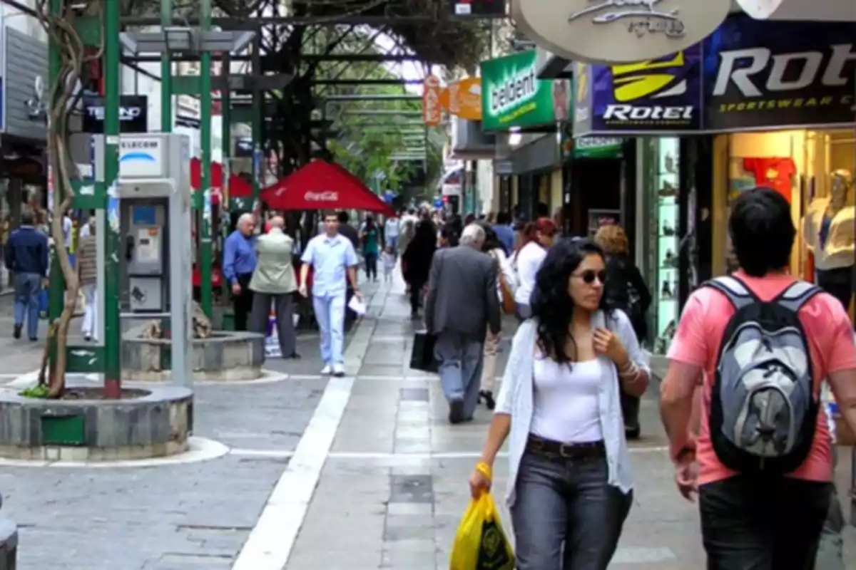 Personas caminando por una calle peatonal comercial con tiendas y carteles a los costados