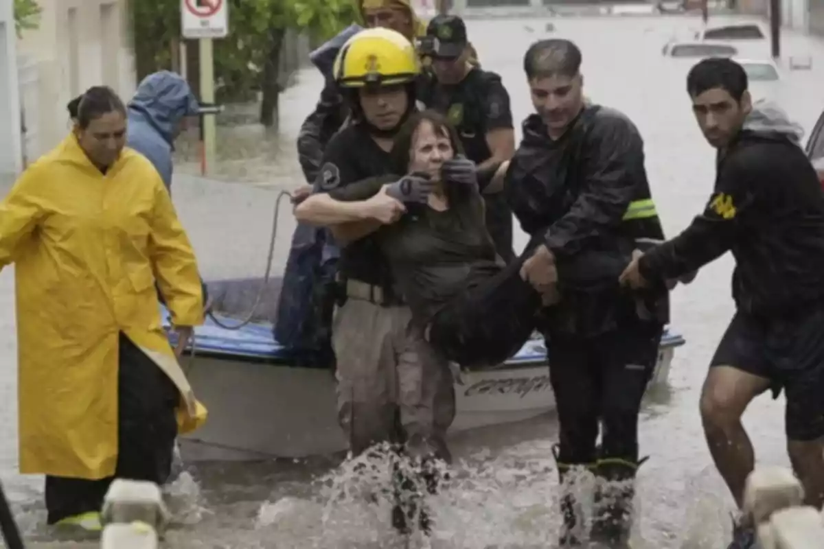 Rescatistas ayudan a una persona durante una inundación, llevándola a un lugar seguro mientras caminan por una calle anegada.