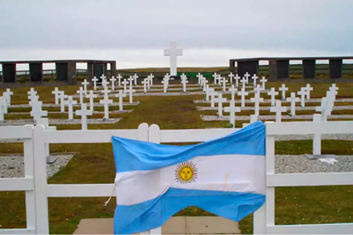 Cementerio militar con cruces blancas y una bandera argentina en primer plano.