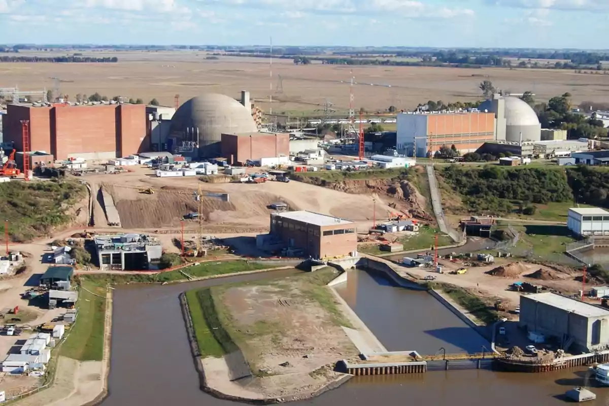 Vista aérea de una planta nuclear rodeada de campos y un canal de agua en primer plano.