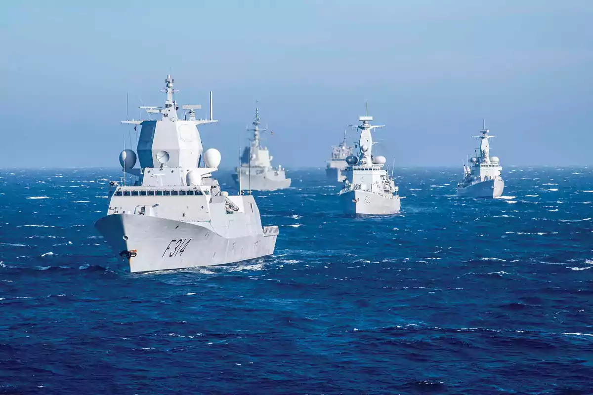 Una formación de barcos de guerra navegando en el océano bajo un cielo despejado.