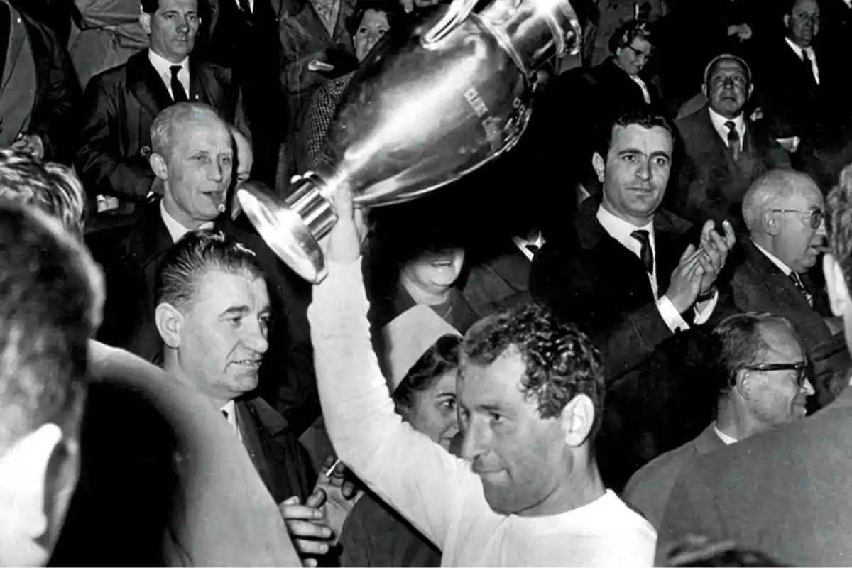 Un jugador de fútbol levanta un trofeo mientras la multitud aplaude y celebra a su alrededor.