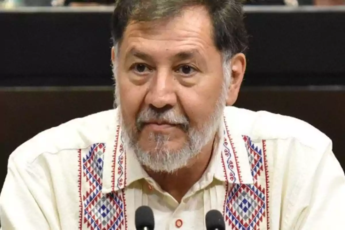 A man with a beard and dark hair is wearing a jersey with colorful embroidery while speaking in front of a microphone.