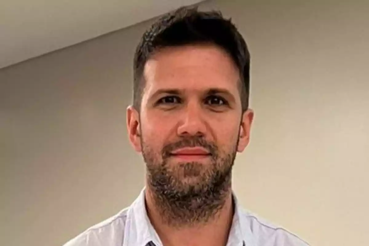 Un hombre con barba y cabello oscuro lleva una camisa clara y mira hacia la cámara con una expresión neutral. Un hombre con barba y cabello oscuro lleva una camisa clara y mira hacia la cámara con una expresión neutral.
