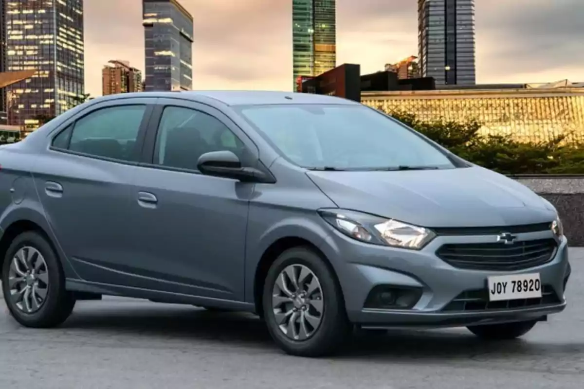 Un automóvil gris estacionado frente a un paisaje urbano con edificios altos al atardecer.