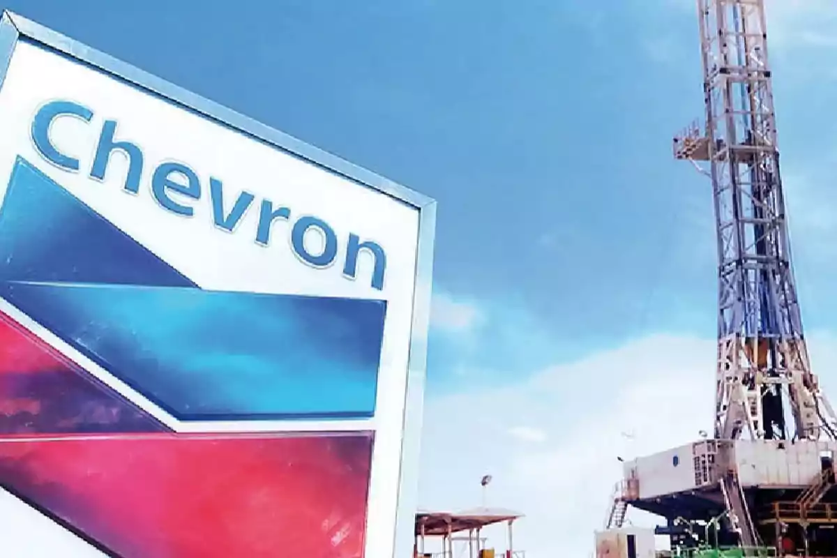 Un letrero de Chevron junto a una torre de perforación bajo un cielo azul.