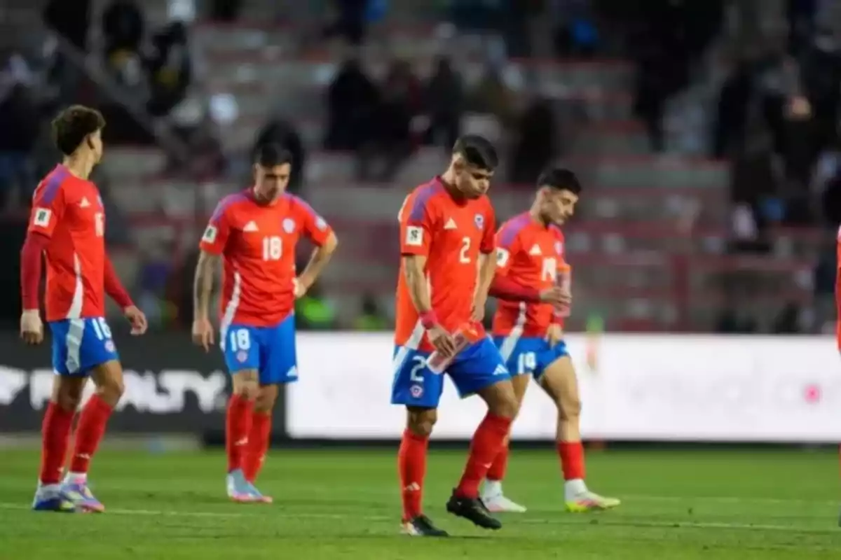 Jugadores de fútbol con uniforme rojo y azul caminan cabizbajos en el campo durante un partido Jugadores de fútbol con uniforme rojo y azul caminan cabizbajos en el campo durante un partido