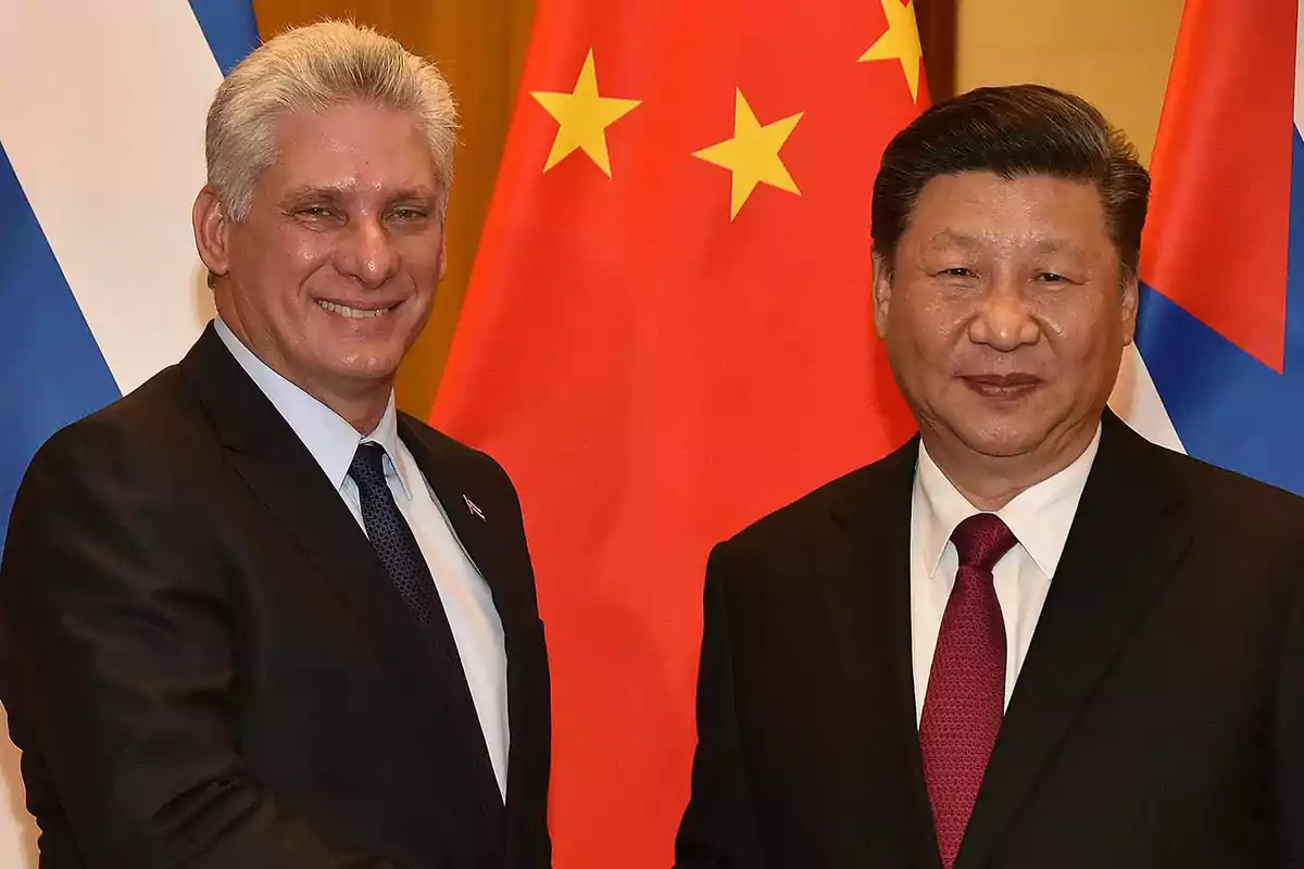 Dos hombres de traje sonríen frente a las banderas de China y Cuba.