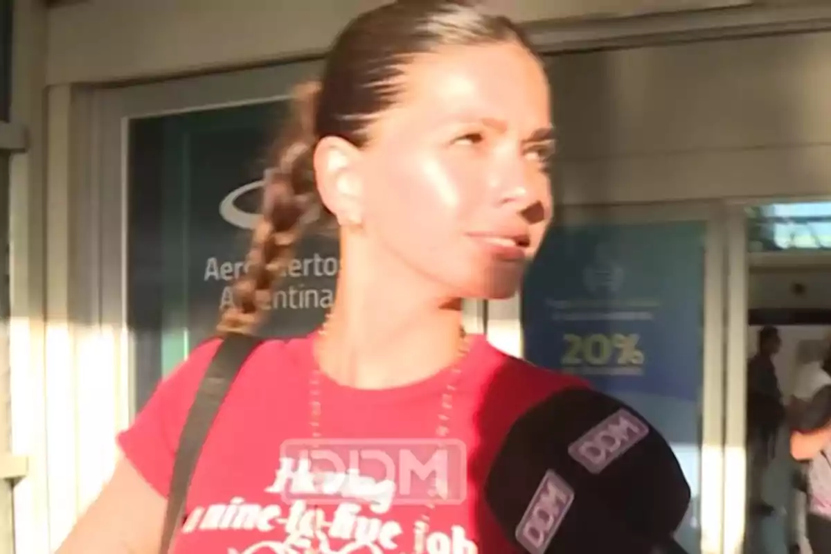 Mujer con camiseta roja siendo entrevistada en un aeropuerto.