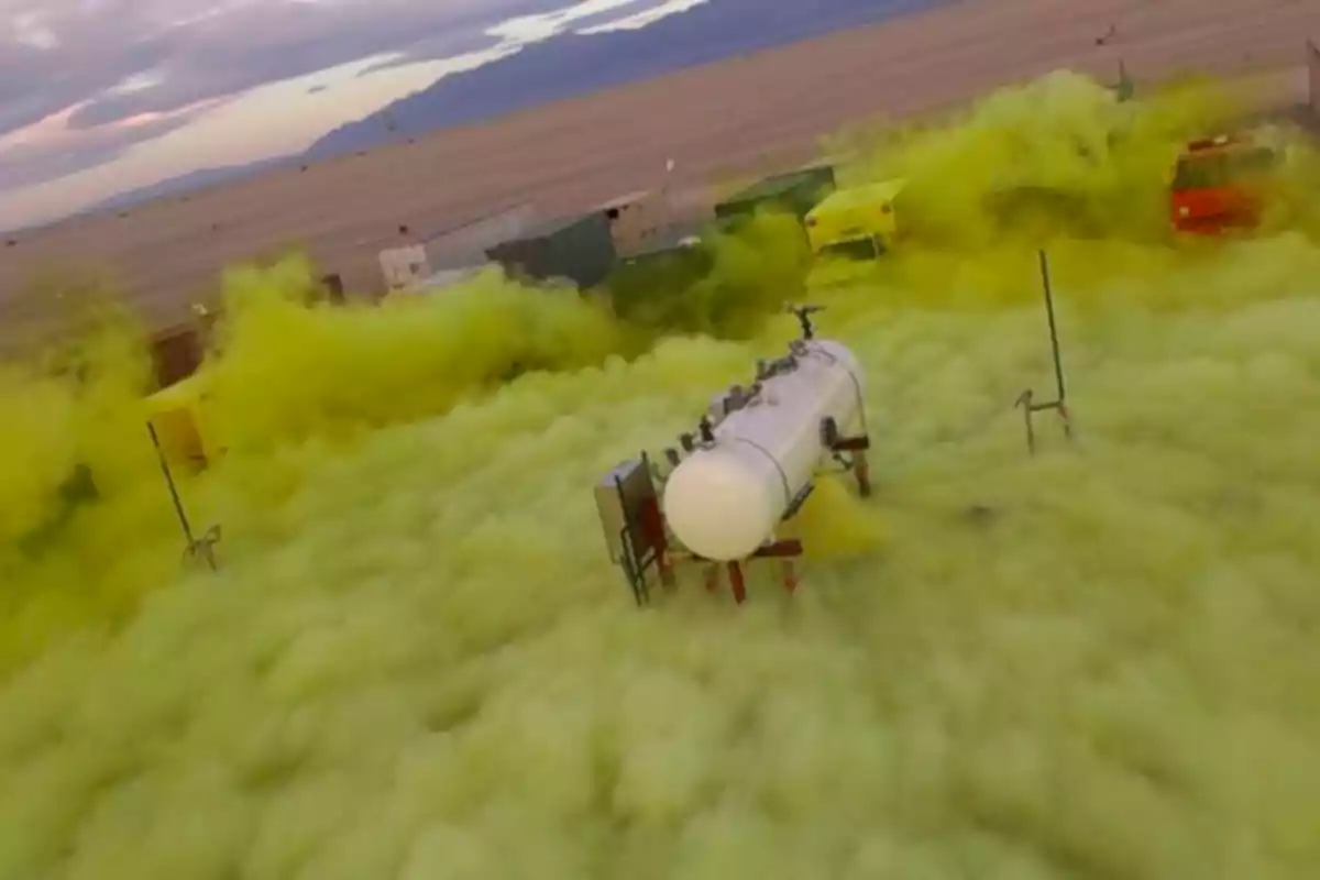 Tanque blanco rodeado de una densa nube de gas amarillo en un área desértica con vehículos y estructuras al fondo Tanque blanco rodeado de una densa nube de gas amarillo en un área desértica con vehículos y estructuras al fondo