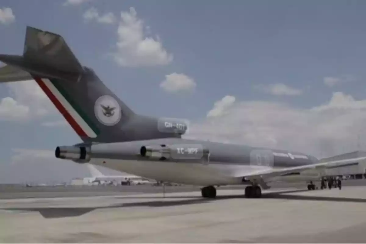 Un avión con la bandera de México en la cola está estacionado en una pista de aterrizaje bajo un cielo parcialmente nublado.