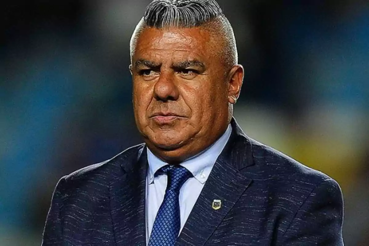 Gray-haired man with slicked-back hair wearing a blue suit and tie in a formal setting