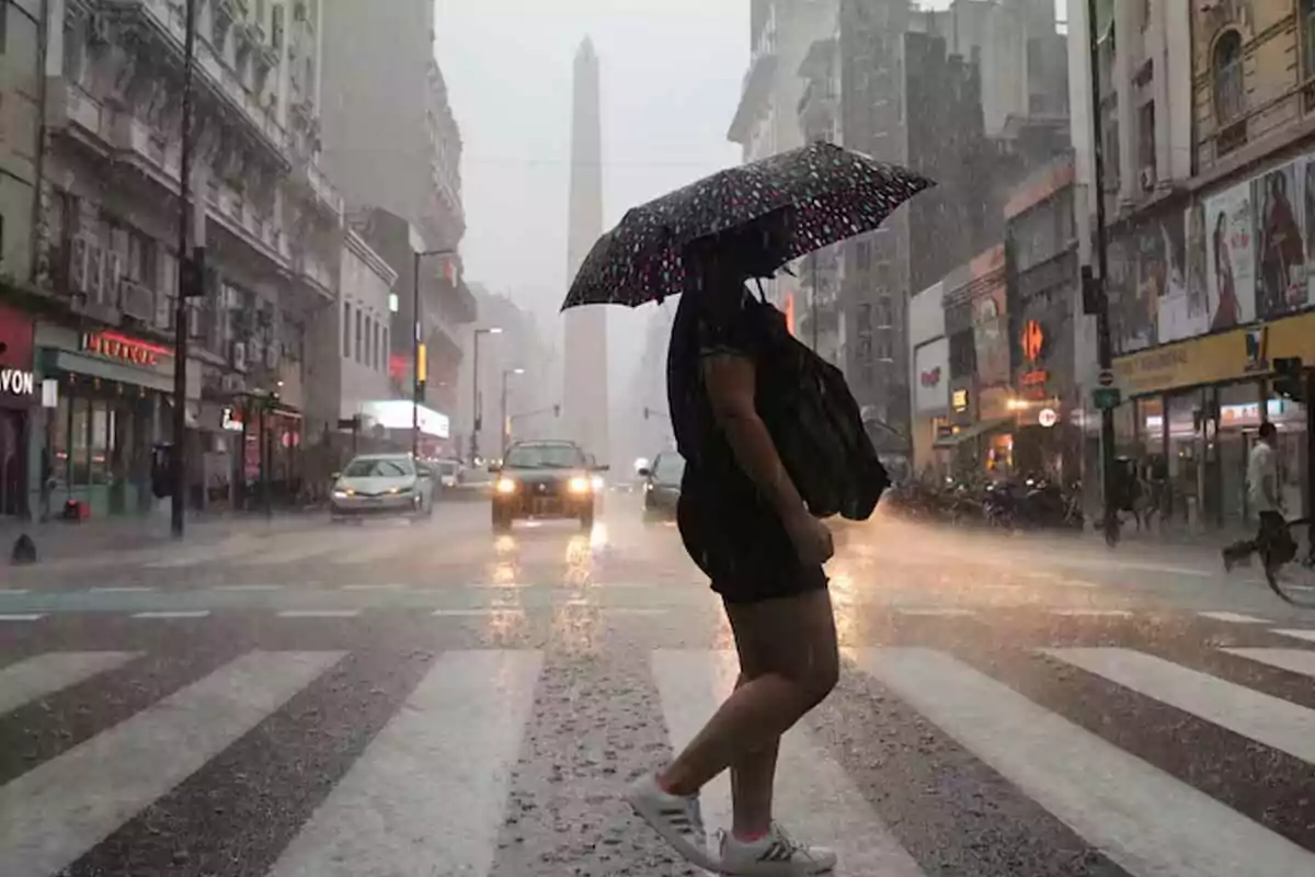 Persona con paraguas cruzando una calle bajo la lluvia intensa en una ciudad con edificios altos y tráfico. Persona con paraguas cruzando una calle bajo la lluvia intensa en una ciudad con edificios altos y tráfico.