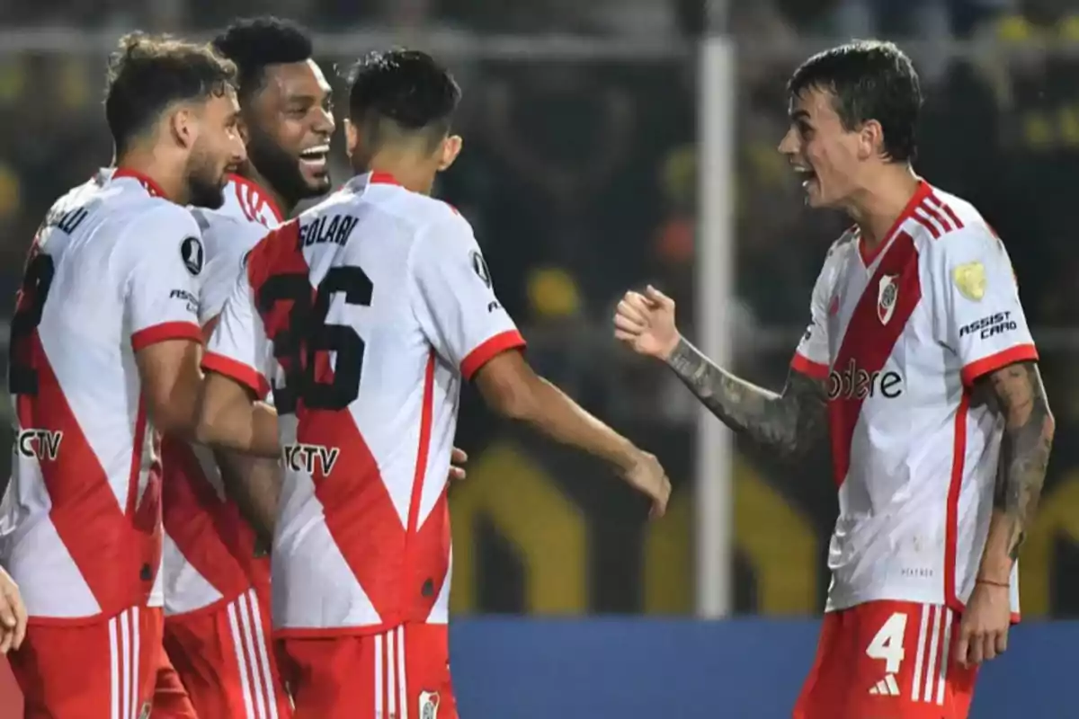 Jugadores de fútbol con uniforme blanco y rojo celebran en el campo.