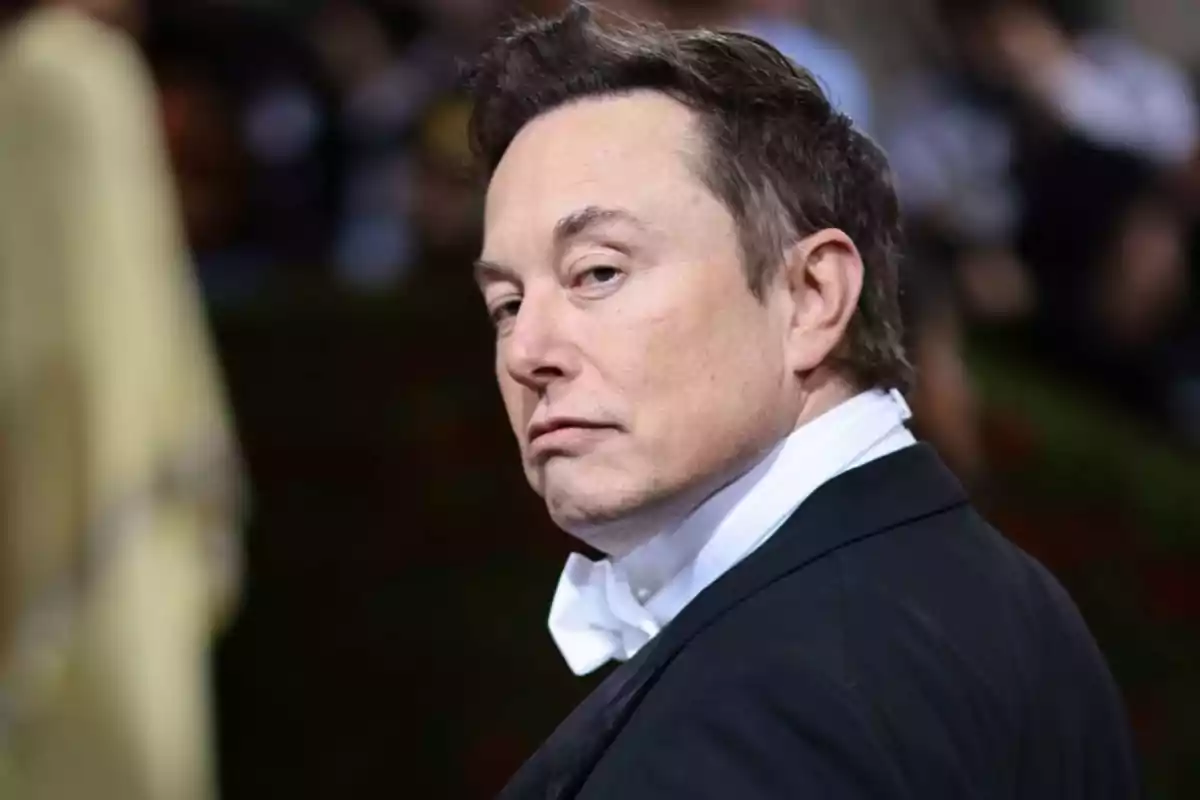 Hombre de cabello corto y oscuro vistiendo esmoquin negro con camisa blanca y pajarita, mirando hacia atrás con expresión seria en un evento elegante Hombre de cabello corto y oscuro vistiendo esmoquin negro con camisa blanca y pajarita, mirando hacia atrás con expresión seria en un evento elegante