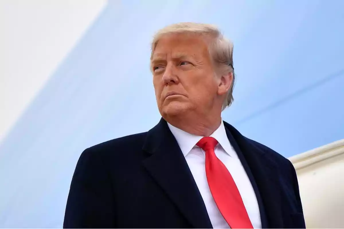 Blond-haired man in a dark suit and red tie looking to the side against a light blue background Blond-haired man in a dark suit and red tie looking to the side against a light blue background