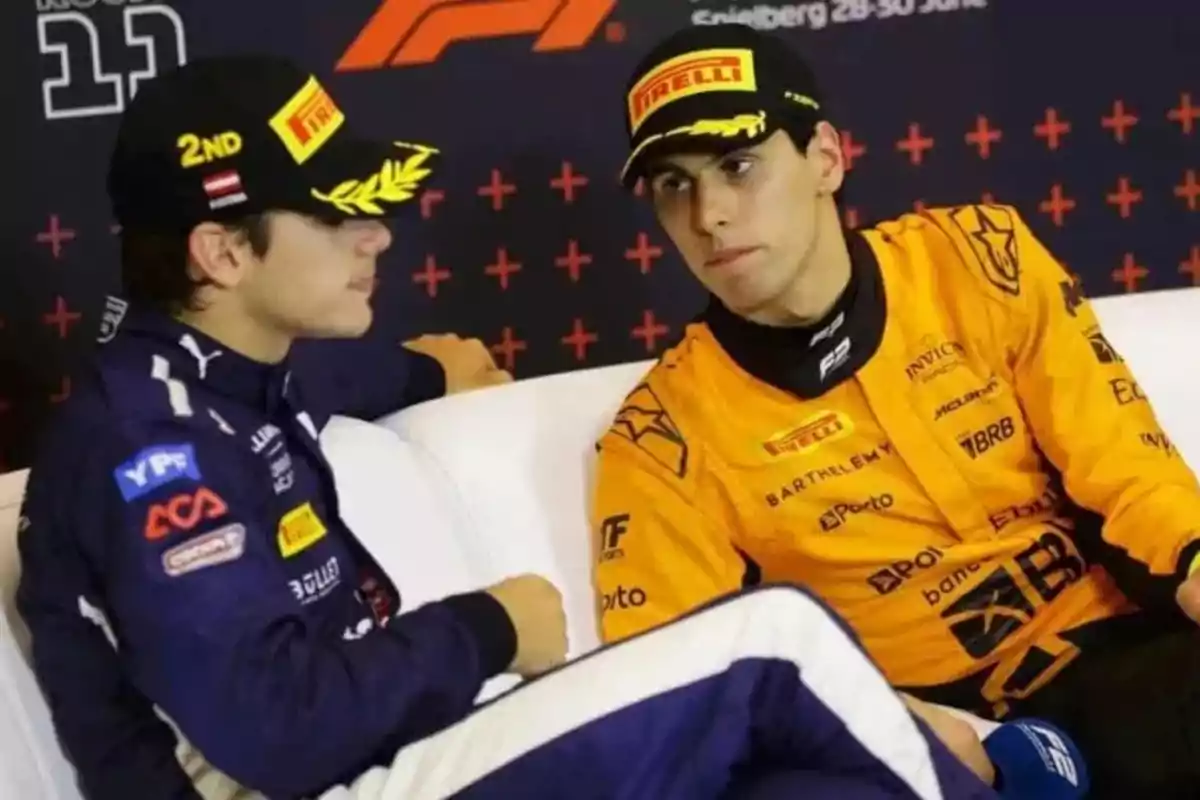 Dos pilotos de carreras con uniformes y gorras de Pirelli conversan en un sofá durante un evento de automovilismo.