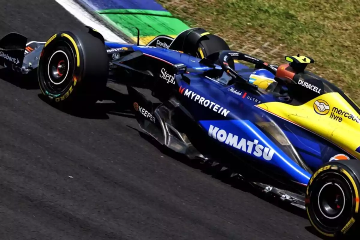 Un auto de carreras de Fórmula 1 en la pista con colores azul y amarillo y varios logotipos de patrocinadores.