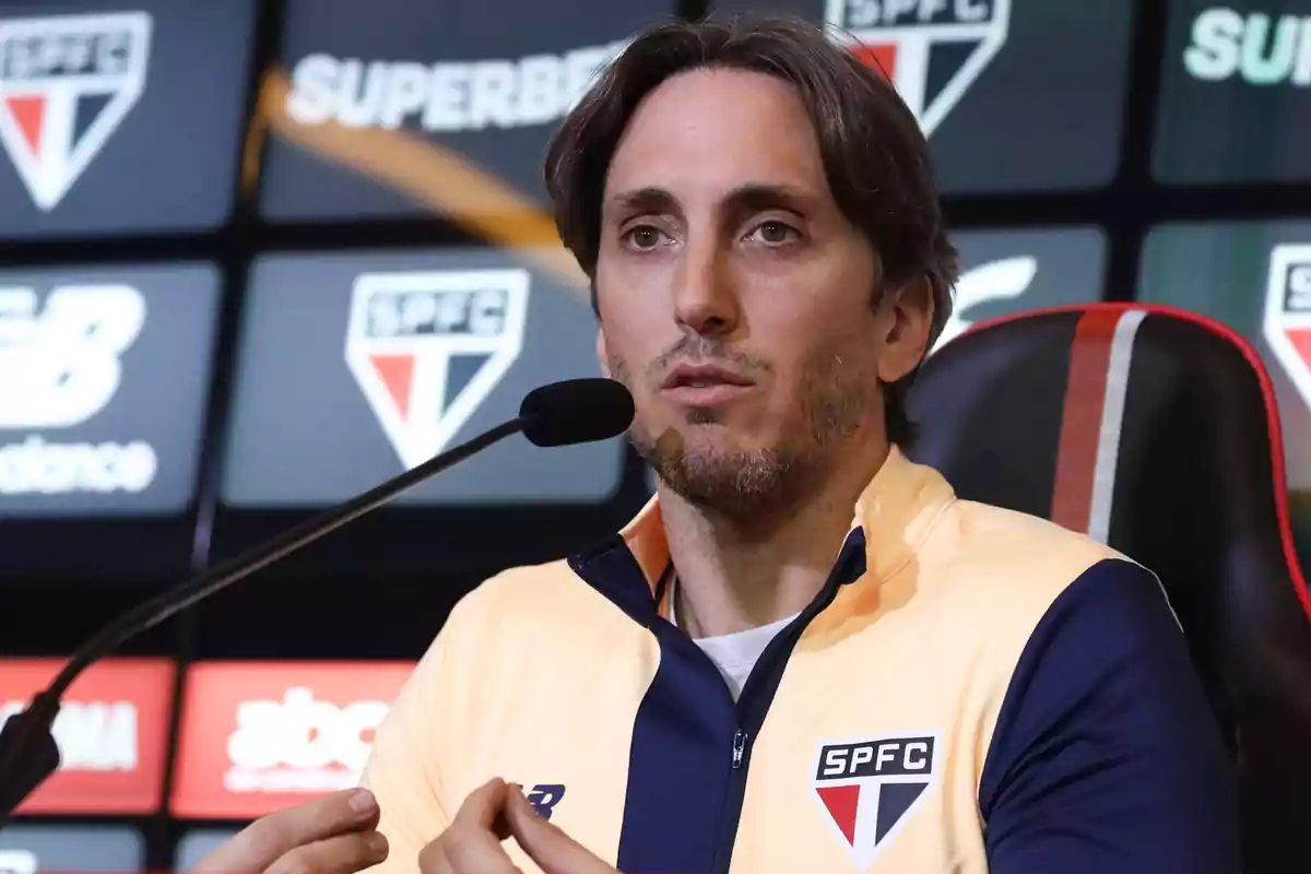 A man speaking at a press conference with a microphone in front of him and a background with SPFC logos. A man speaking at a press conference with a microphone in front of him and a background with SPFC logos.