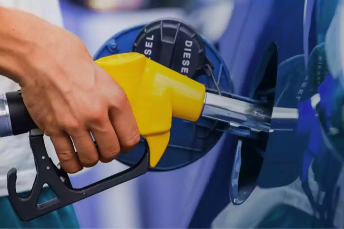Una mano sosteniendo una manguera de combustible amarilla mientras llena el tanque de un vehículo diésel.