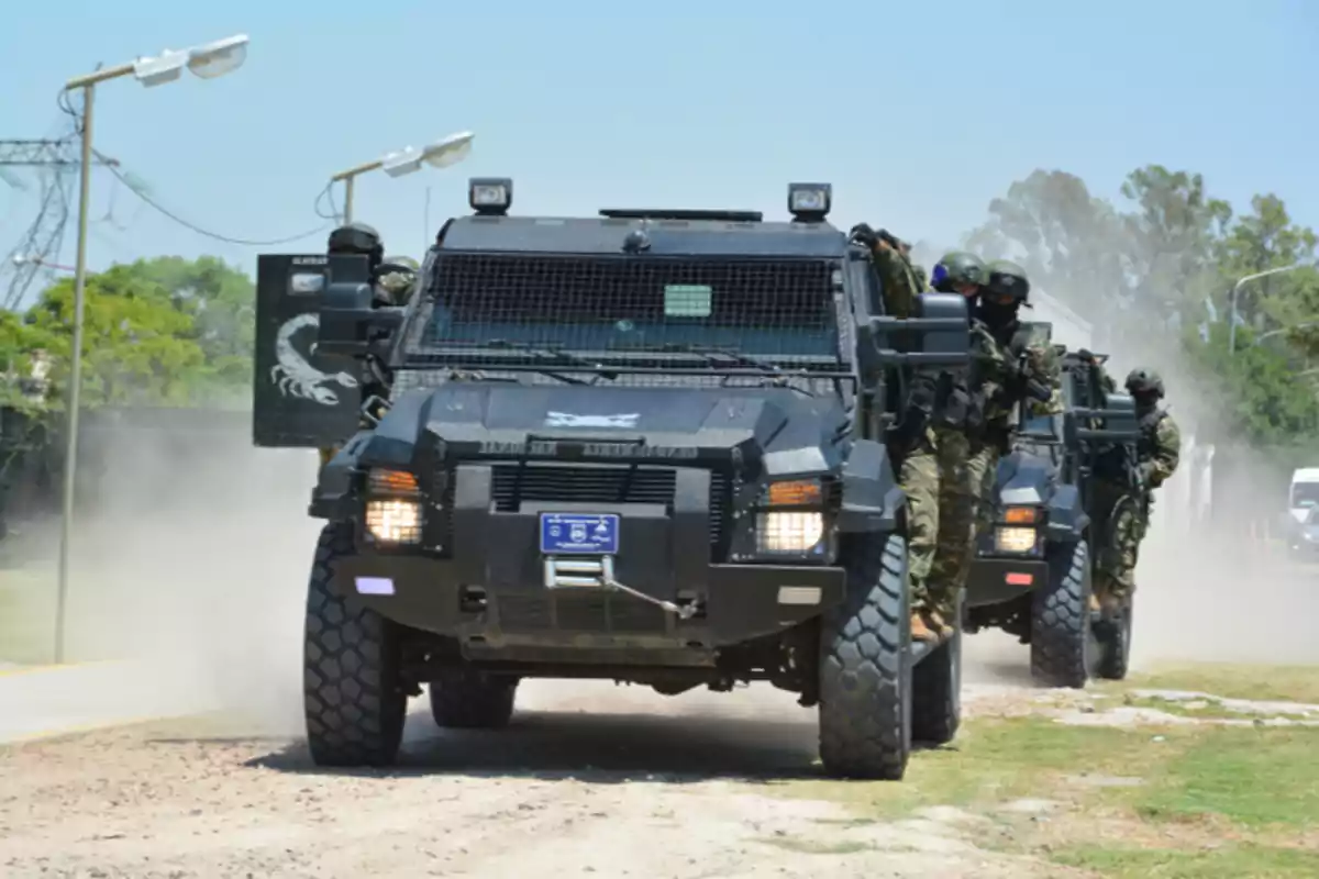 Vehículos blindados avanzando por un camino polvoriento con soldados equipados en sus laterales.