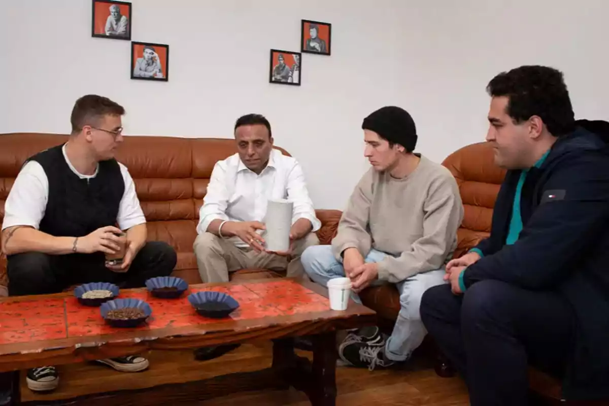 Un grupo de personas sentadas en un sofá alrededor de una mesa con muestras de café, mientras una de ellas sostiene un objeto cilíndrico. Un grupo de personas sentadas en un sofá alrededor de una mesa con muestras de café, mientras una de ellas sostiene un objeto cilíndrico.