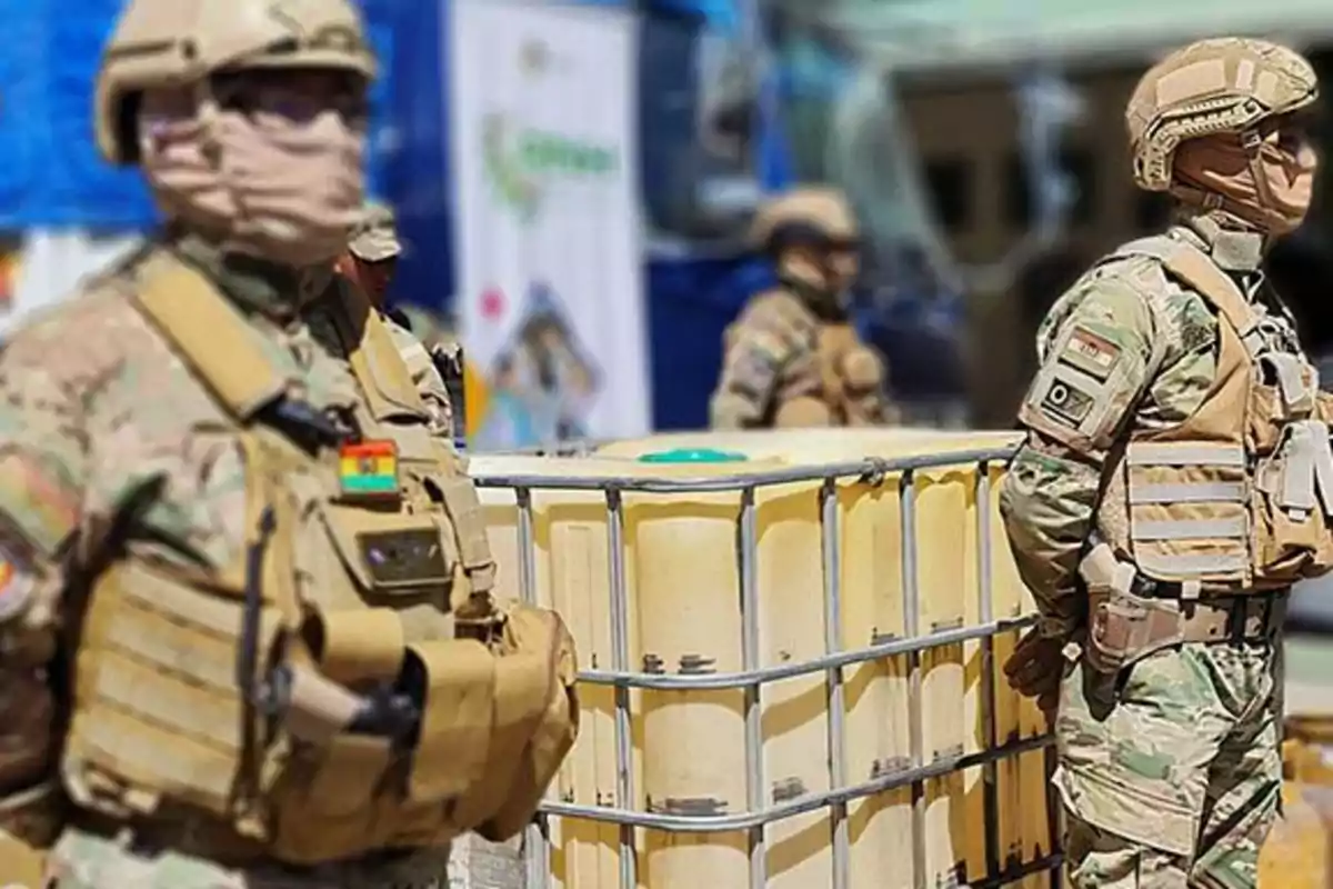 Soldados con uniformes de camuflaje y cascos protegen un contenedor grande en un entorno urbano.