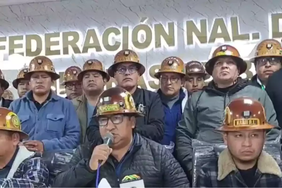 Un grupo de personas con cascos de minero se encuentra reunido en una sala, uno de ellos sostiene un micrófono mientras habla. Un grupo de personas con cascos de minero se encuentra reunido en una sala, uno de ellos sostiene un micrófono mientras habla.